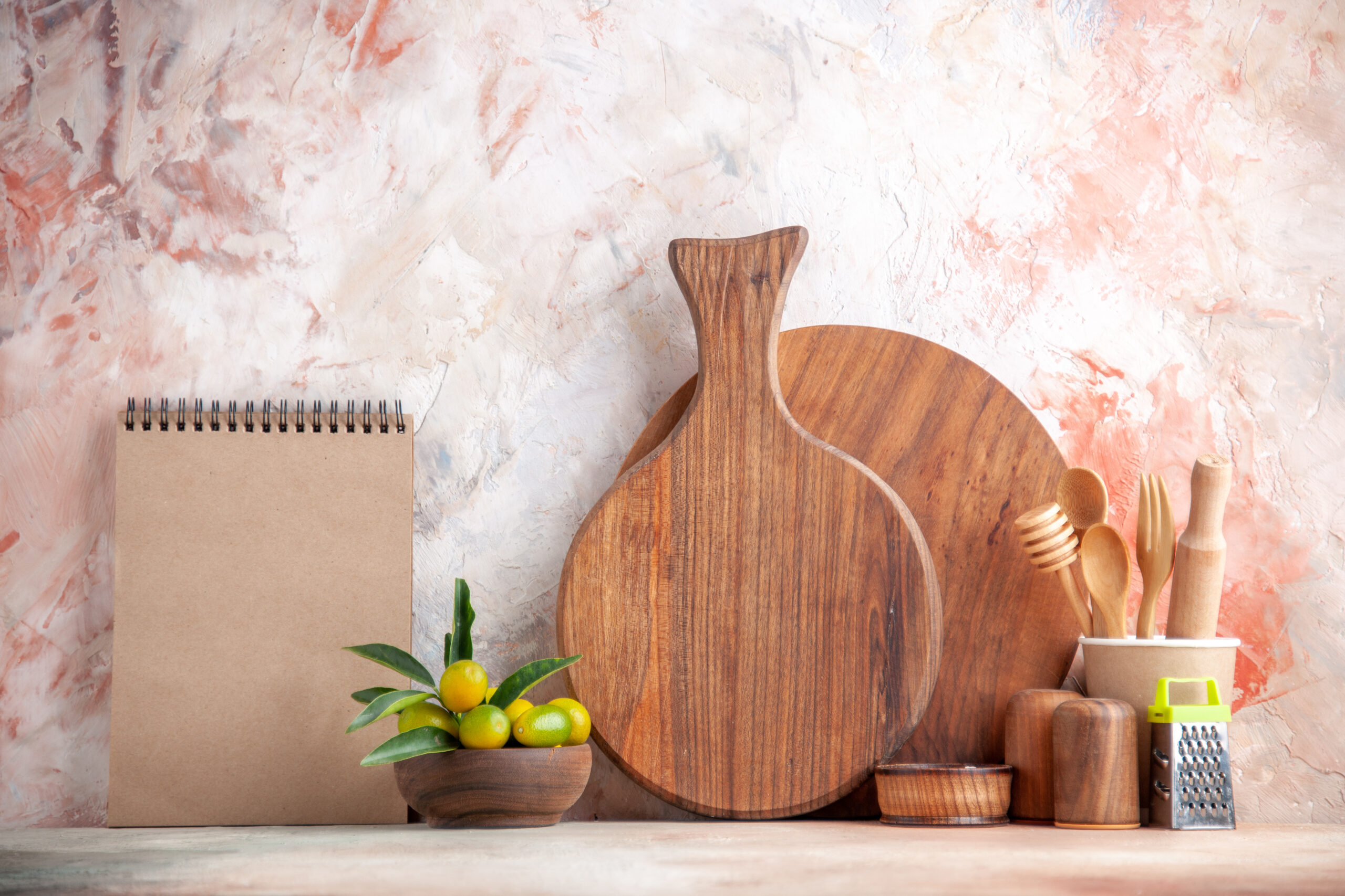 front-close-view-cutting-board-wooden-spoons-grater-kumquats-pot-notebook-colorful-surface